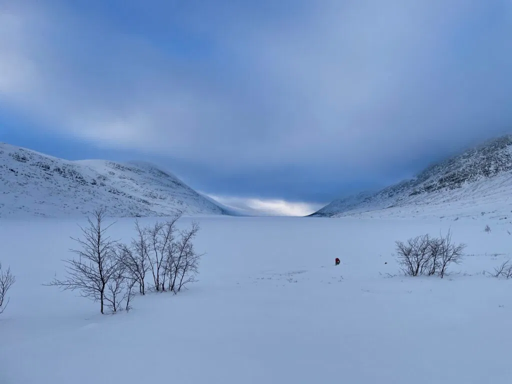 Zugeschneiter See zwischen zwei Bergen auf einer Schneemobiltour.