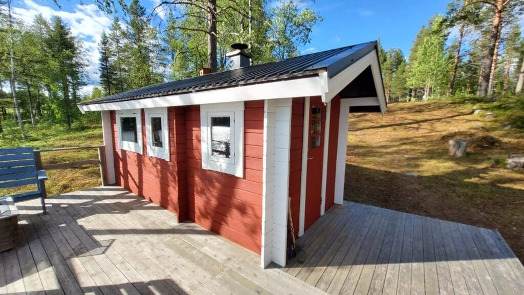klassisches rotes schwedisches Saunahaus am See bei strahlendem Sonnenschein in Abborrträsk, Norrbotten.